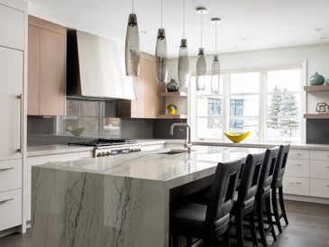 Elegant kitchen with marble kitchen island and five glass pendants hanging above.