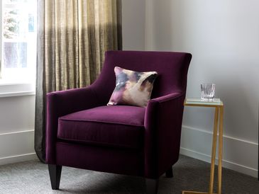 Custom linen drapery next to a purple arm chair with toss cushion.