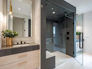Bathroom with blonde wood vanity, gray quartz countertop next to large steam shower with bench.