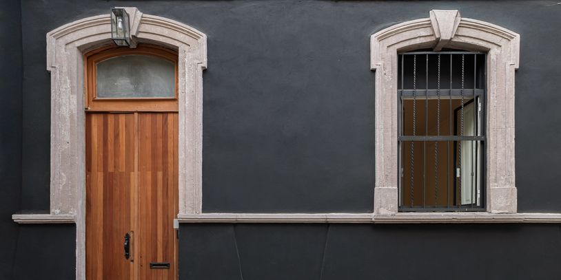 Puerta de madera y ventana con barrotes en pared negra.