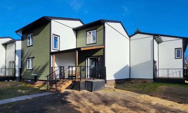 Modern duplex with green and white siding under clear blue sky.