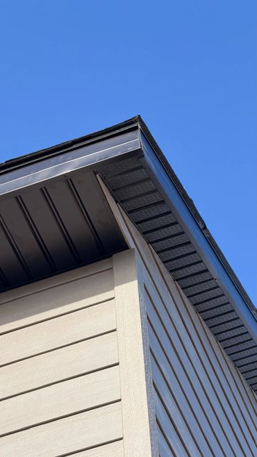 Upward view of a house corner with clean siding and blue sky.