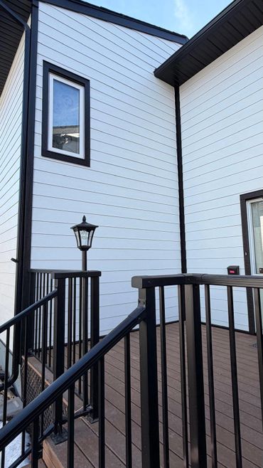 Modern house exterior with white siding and black trim, featuring a wooden deck and black metal railing.