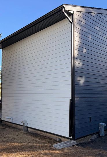 Modern house corner with contrasting white and dark siding under a clear blue sky.