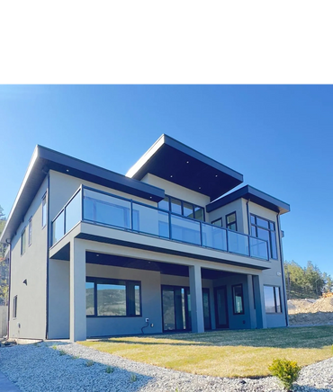 Modern two-story house with glass balcony and flat roof under clear blue sky.