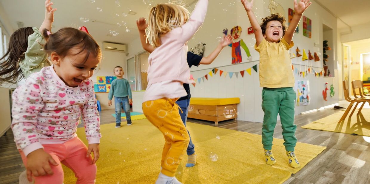 Children joyfully playing with bubbles indoors on a yellow carpet.