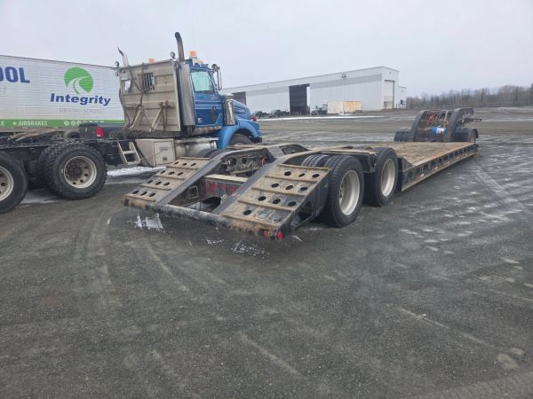 Heavy-duty blue truck with a lowboy trailer in an industrial yard.