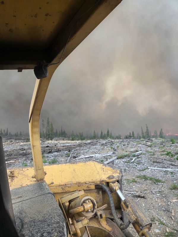 View from inside a bulldozer clearing land amid a smoky forest fire.