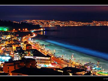 A vibrant coastal city illuminated at night with glowing beaches and bright city lights.