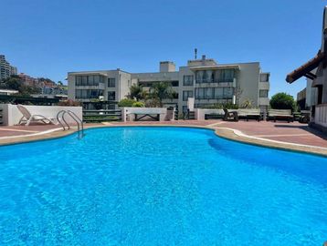 Outdoor swimming pool with clear blue water and lounge chairs on a sunny day.