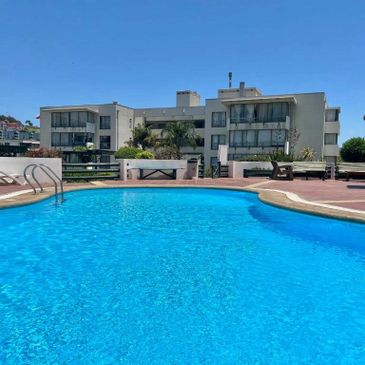 Outdoor swimming pool with clear blue water and lounge chairs on a sunny day.