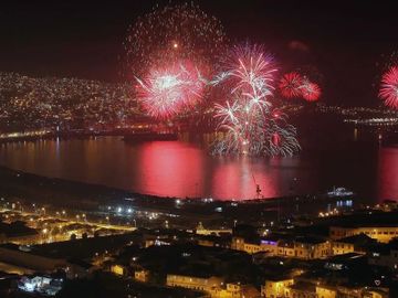 Fireworks light up the night sky over a city harbor reflecting vibrant colors on the water.