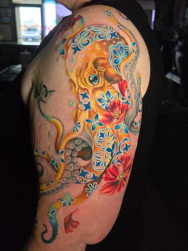 Colorful octopus tattoo with blue floral patterns and red flowers on upper arm.