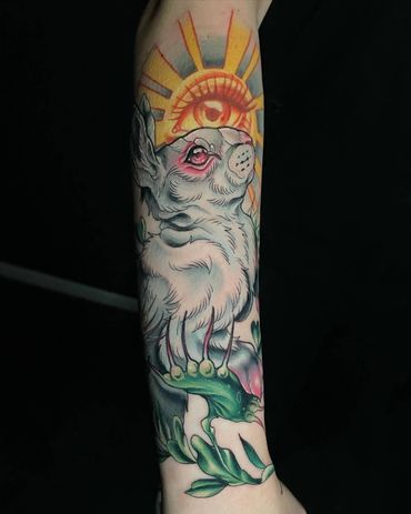 Tattoo of a rabbit with an eye and sun rays above it on a person's arm.