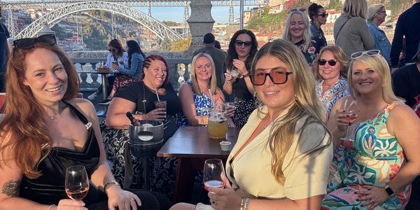 Group of women enjoying drinks outdoors with a bridge in the background.