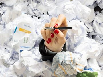 Hand of a business professional buried under a pile of crumpled up paper.