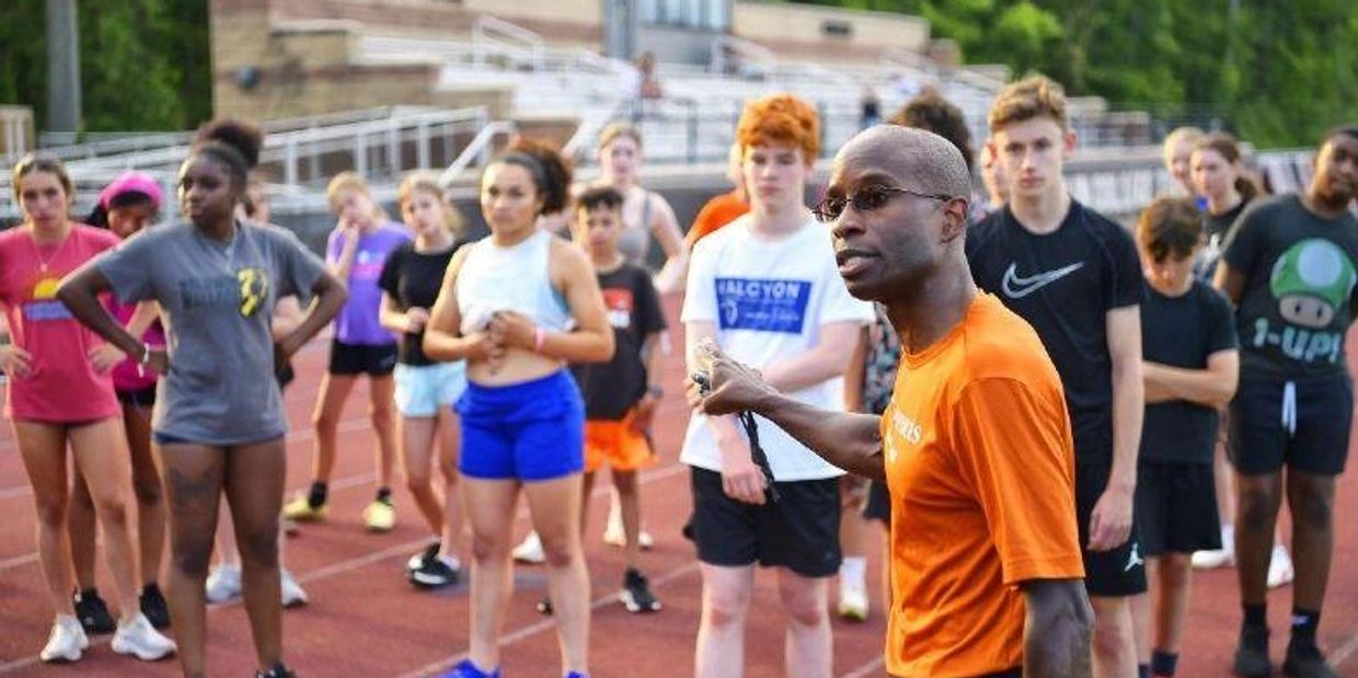 Coach giving instructions to a group of young athletes on a running track.
