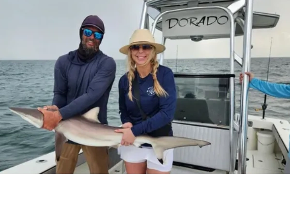 couple holding spinner shark while shark fishing