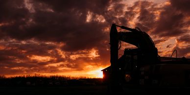 Silhouette of construction equipment against a dramatic sunset sky.
