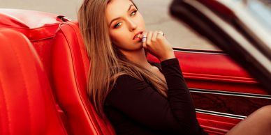 Young woman with long hair sitting in a red car interior, looking thoughtfully.