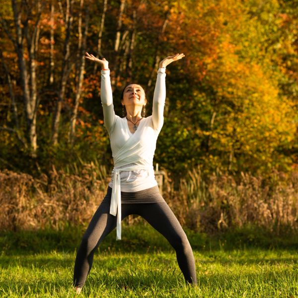 Woman practicing yoga outdoors in autumn, arms raised.