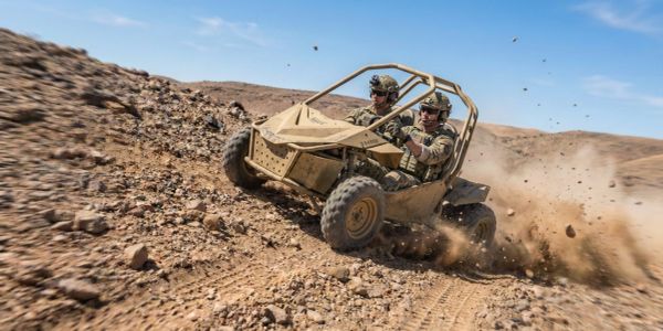 Two soldiers driving a dune buggy across rocky terrain.