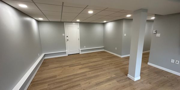 Empty modern basement with wooden floor and grey walls.