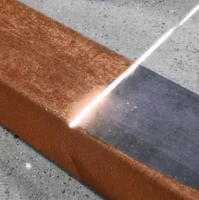 A laser cutting through a rusty metal beam, revealing clean metal beneath.