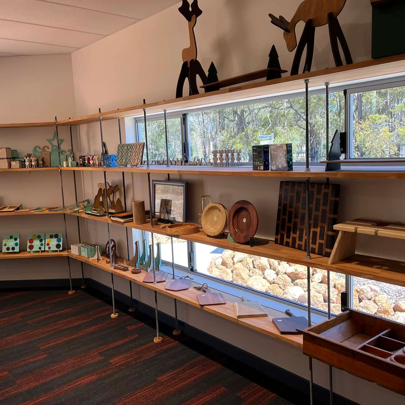 Wooden art and craft pieces displayed on shelves in a bright room with windows.
