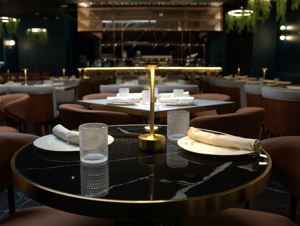 Elegant restaurant table setting with black marble top and golden lamp.