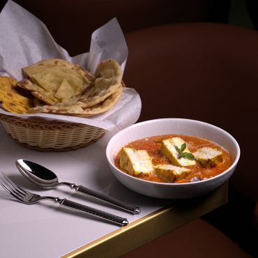 Indian paneer curry with naan bread and cutlery on a white table.