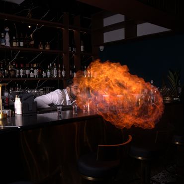 Bartender performing a fire-breathing stunt at a dimly lit bar.