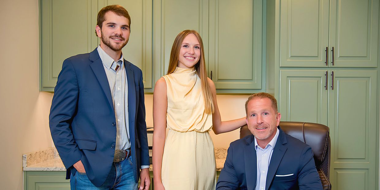 Three people posing indoors, two standing and one seated.
