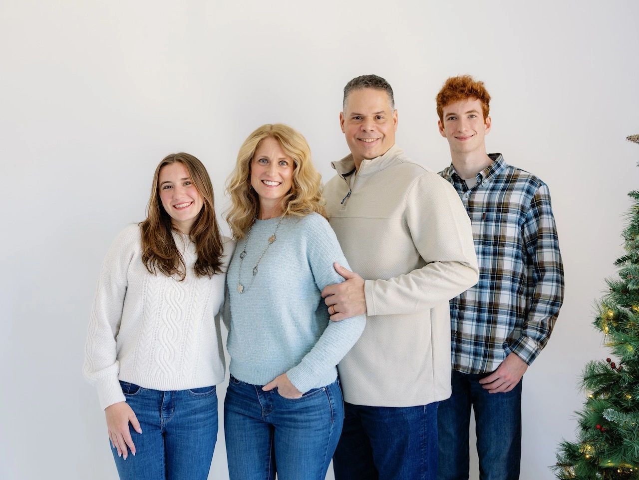 Smiling family of four posing together beside a Christmas tree.