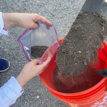 Hands putting soil into a plastic zipper bag over a red bucket.