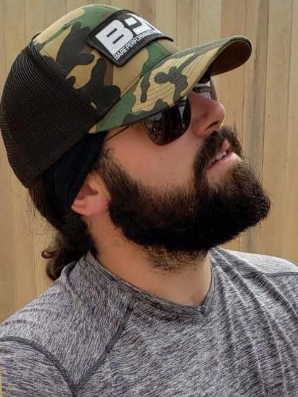 Man with beard, sunglasses, and camo hat looking up.