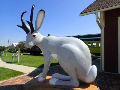 Large jackalope statue outdoors near a train.