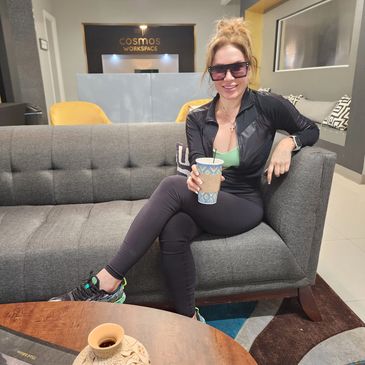 Lady smiling holding a coffee cup sitting on a couch coworking in the open community space.