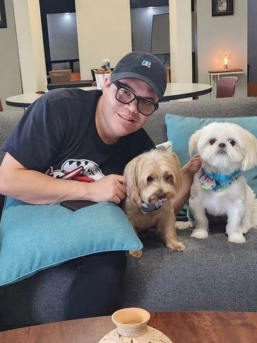 Hervin Hidalgo smiling sitting on sofa with dogs.