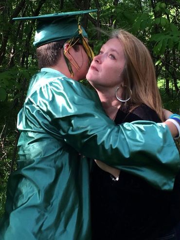 Son with high school graduation robe hugging mom.