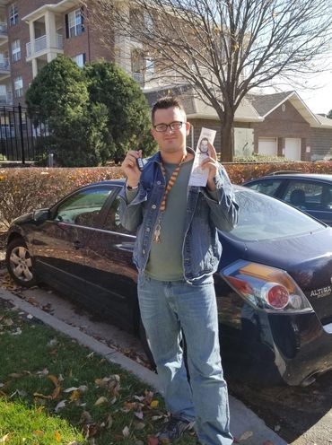 Young man standing in front of car with a drivers license and car key.