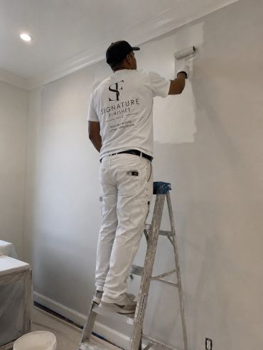 Man painting a wall using a roller on a ladder.