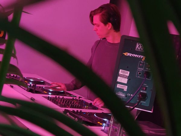DJ playing music behind equipment bathed in pink light.