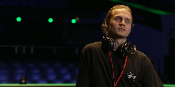 A man with headphones around his neck stands in a dimly lit room.