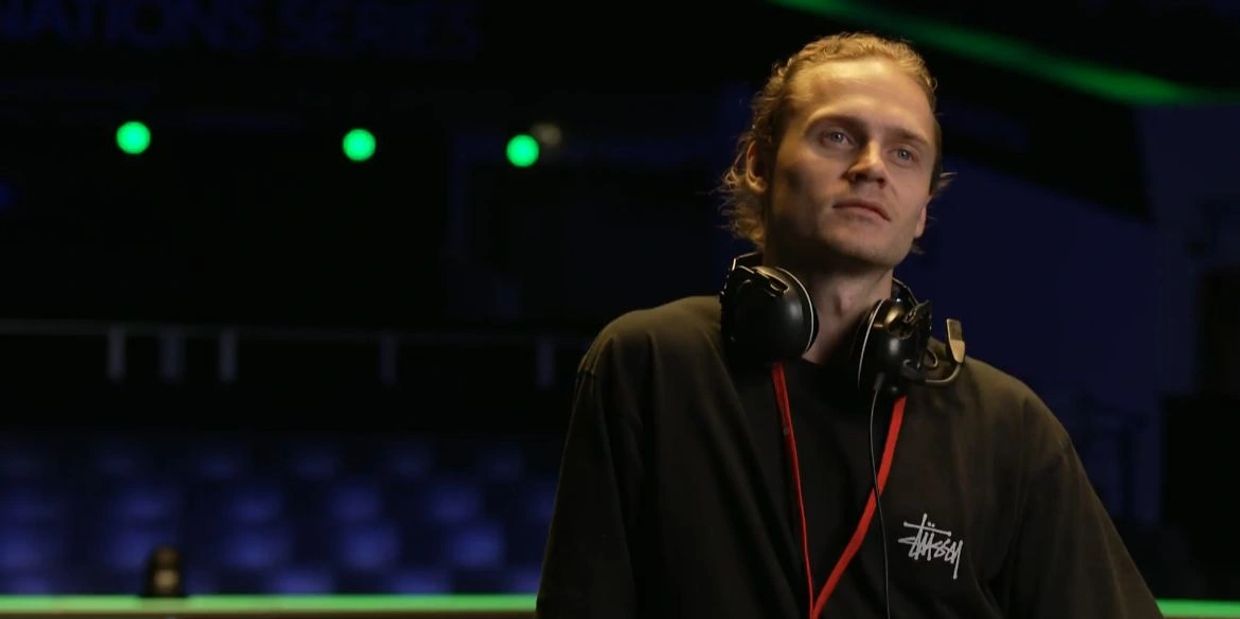 Man with headphones around neck looking thoughtful in a dimly lit room.
