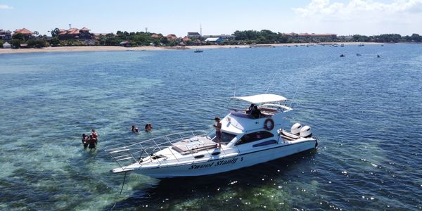 Boat anchored near the shore with people swimming.