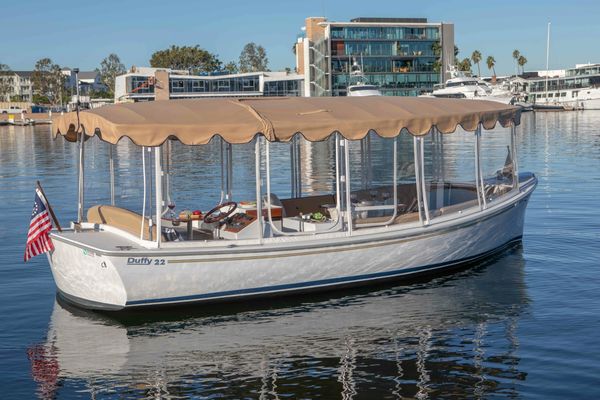 A covered white boat on calm water near buildings.