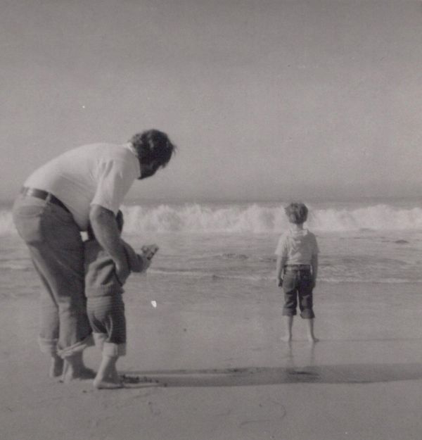 A man and two children at the beach, looking at the ocean waves.
