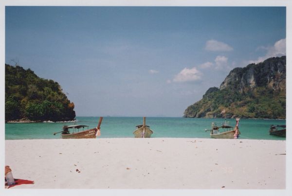 Traditional boats anchored near a white sandy beach with clear blue water.