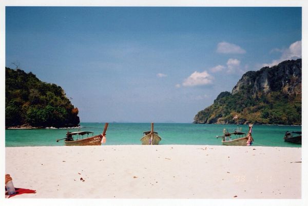 Traditional longtail boats anchored near a pristine white sandy beach with clear turquoise water.